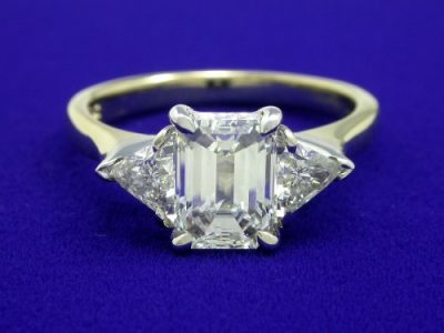 1.32-carat emerald cut diamond graded H color, VS1 clarity and pair of triangular cut diamonds having 0.46 total carat weight in white-gold baskets on a yellow-gold shank 