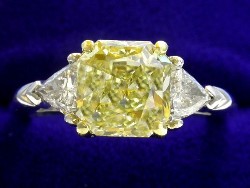 2.06 carat Square Radiant Cut diamond with Fancy Yellow color, VS1 clarity, and 0.40 total carat weight of Trillion side diamonds in platinum and 18-karat yellow gold custom mounting.